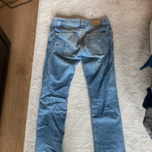 Ljusblå jeans från Nudie Jeans - Säljer ett par ljusblå jeans från Nudie Jeans i modellen W31 L32. Jeansen är tillverkade av 100% ekologisk bomull och har klassisk femficksdesign, orangea sömmar och en snygg tvättad look. Perfekta för dig som gillar en avslappnad och stilren vibe.