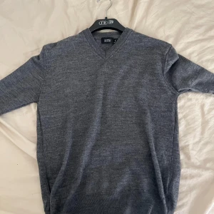 Grå v-ringad tröja från Long Island - Mysig grå v-ringad tröja från Long Island i storlek M. Tröjan har lång ärm och är tillverkad i ett mjukt stickat material som passar perfekt till lager-på-lager. Enkel och stilren design som funkar till många olika looks.