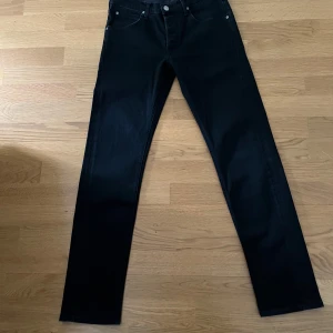Svarta Lee Daren jeans W31 L32 - Svarta jeans från Lee, modell Daren Button Fly. Klassisk femficksdesign, raka ben och normal passform. Jeansen är tillverkade i bomull med en snygg svart tvätt och diskret Lee-logga bak på linningen.