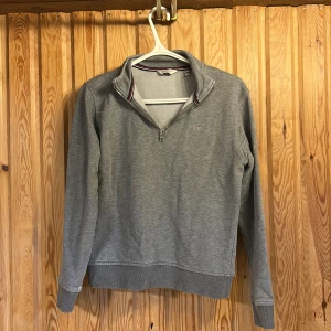 Grå half zip tröja från GANT - Snygg grå långärmad tröja från GANT med halv dragkedja och broderad logga på bröstet. Tröjan har ribbade muddar och en klassisk krage med randig detalj på insidan. Perfekt för lager-på-lager och chill stil.