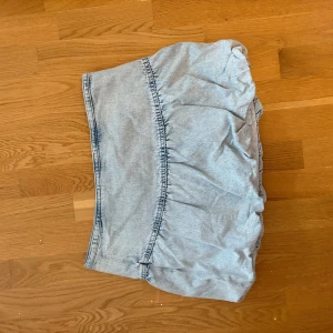 Ljusblå jeanskjol från Pull&Bear - Supersöt ljusblå jeanskjol från Pull&Bear i storlek L men passar M. Kjolen är kort, har en volangig och lätt puffig form med markerad söm i midjan. 