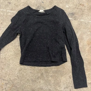 Svart prickig långärmad tröja H&M - Svart långärmad tröja från H&M med vita prickar över hela tyget. Tröjan har en klassisk rund halsringning och är gjord i mjuk bomull, perfekt för en chill och stilren look.