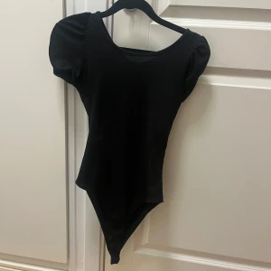 Svart ribbad body med puffärm XS - Svart ribbad body med rund halsringning och korta puffärmar. Tight passform som framhäver siluetten och ger en clean look. Perfekt att styla med jeans eller kjol för en trendig vibe. Den är jätte snygg men tyvärr liten för mig. Köpte den på myrorna 🥰