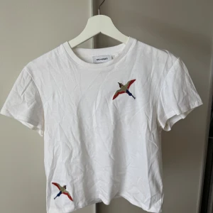 Vit t-shirt med broderad fågel Axel Arigato - Vit t-shirt från Axel Arigato med två broderade fåglar i färg på bröstet och nedtill. Klassisk rund hals och korta ärmar. Skön passform och stilren design som sticker ut med de färgglada detaljerna. Mycket bra skick☺️ Nypris ca 1000kr 