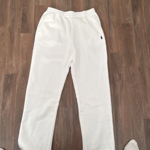 Vita mjukisbyxor från Ralph Lauren - Vita mjukisbyxor från Ralph Lauren med klassisk svart broderad logga på ena benet. Byxorna har resår i midjan och är gjorda i mjuk bomullsmix med fleeceinsida. Perfekta för chill dagar eller när du vill ha en clean och stilren look.