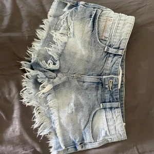 Ljusblå jeansshorts med fransar - Snygga ljusblå jeansshorts från Zara med slitna detaljer och långa fransar längs benen. Klassisk femficksmodell och låg midja. Perfekta för sommaren och ger en cool, avslappnad vibe.