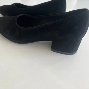 Svarta mockapumps från Vagabond - Klassiska svarta pumps från Vagabond i mjuk mocka med rund tå och låg, bred klack. Snygg och enkel design som passar till många olika outfits. Perfekta för dig som gillar stilrena och bekväma skor med en modern touch. Använda fåtal ggr. Mycket gott skick 