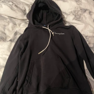 Svart Champion hoodie med broderad logga - Svart hoodie från Champion med broderad logga på bröstet och ärmen. Klassisk känguruficka framtill, vita snören i huvan och ribbade muddar. Jätteskön men använder den aldrig har cirka använt den 4 gånger det är storlek M men är väldigt liten i storleken så de passar även på S/xs pris kan även diskuteras mer.