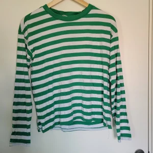 Randig långärmad tröja - Grön och vit randig långärmad tröja från Monki i storlek S. Tröjan har en klassisk rund halsringning och är tillverkad i en mjuk mix av bomull och modal, vilket gör den superbekväm.