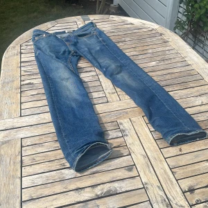 Blå jeansbyxor från Lager 157 - Klassiska blå Lager 157jeans med raka ben och snyggt slitna detaljer. Jeansen har fem fickor, gylf med knappar och den ikoniska läderpatchen bak i midjan. Perfekta för en avslappnad och tidlös stil.