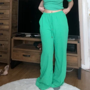 Gröna wideleg byxor från Sisters Point - Snygga gröna mjukis-/kostym-byxor från Sisters Point i storlek L. Byxorna har bred resår i midjan med snörning och vida ben för en chill och trendig look. Perfekta för dig som gillar bekväma och stilrena plagg. Materialet känns mjukt och följsamt. Innerbenslängd: 78 cm, midjevidd: 37 cm, stussvidd: 54 cm.