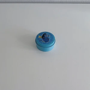 Hitta Nemo ask - En blå liten Hitta Nemo ask  i metall/plåt som är i använt skick och har en del skavanker som man ser på bilderna (locket är trögt att ta av)! FÖRST TILL KVARN!