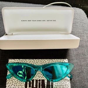 Turkosa cat eye-solglasögon från Chimi - Snygga cat eye-solglasögon från Chimi i transparent turkos plast med spegelblå linser. Ramen har en cool, modern form och logga på skalmen. Perfekta för dig som vill sticka ut med en färgstark accessoar. Fodral och putsduk medföljer.