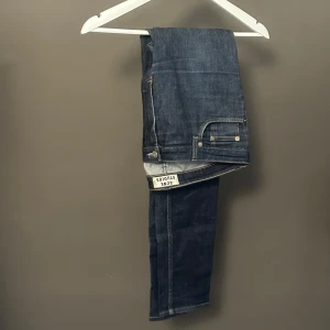 Acne Studios Flex S Raw jeans blå - Snygga mörkblå jeans från Acne Studios, modell Flex S Raw. Klassisk femficksdesign, raka ben och diskreta kontrastsömmar. Tillverkade i bomull med lite stretch för extra komfort. Perfekta för dig som gillar stilrena och tidlösa jeans.