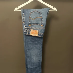 Blå Slim jeans från Jacob Cohen - Snygga blå jeans från Jacob Cohen med klassiska orange sömmar och patch bak. Modellen är skinny fit med normal midja och tillverkad i mjukt jeanstyg. Perfekta för dig som gillar en tajt passform och stilren look.