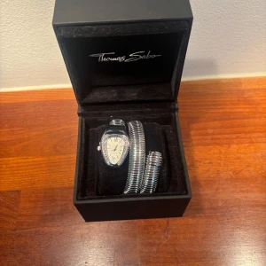 Silverfärgad ormklocka - Snygg och unik klocka med spiralformad, silverfärgad metallarmband som slingrar sig runt handleden. Urtavlan är droppformad med romerska siffror och glittrande stenar runt kanten. Perfekt för dig som vill sticka ut med din stil. Extra batteri medföljer. Klockbox ej inkluderad