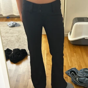 Svarta kostymbyxor från RYVLS - Snygga svarta kostymbyxor från RYVLS (kidzbrandstore) med två knappar framtill och hällor för bälte. Byxorna är booth cut och fuskfickor bak. Jätte fina byxor! Dom är LOW WAIST