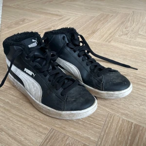 Svarta Puma sneakers med foder - Svarta höga sneakers från Puma med vit sidodetalj och logga. Skorna har svart snörning, vit sula och mjukt svart foder runt ankeln för extra komfort. Ovandelen är i skinn och mocka, perfekt för kyligare dagar. Om man funderar på att köpa så kommer jag städa som innan dom skickas.