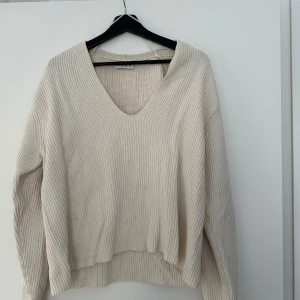 Beige stickad v-ringad tröja Wera - Supermysig beige stickad tröja från Wera med v-ringning och lång ärm. Tröjan har en relaxed passform och ribbad struktur som ger en chill vibe. Perfekt att slänga på sig när det är lite kyligt ute.