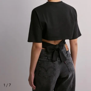 Svart croppad topp med knyt i ryggen - Säljer en svart croppad topp med korta ärmar och snygg knytning i ryggen. Toppen har en enkel och stilren design med rund halsringning och öppen rygg. Perfekt för dig som gillar trendiga och bekväma plagg med det lilla extra.