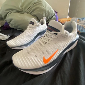Nike React Intinity run 4 - Nike React sneakers i vitt med en snygg orange swoosh på sidan. Ovandelen är stickad och ventilerande, med grå detaljer längs sulan och svart yttersula. Skorna har vart använda några gånger men säljer pga dom har blivit för små. Ny pris på de är 2000     Pris kan diskuteras.