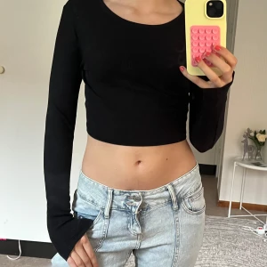 Svart croppad långärmad topp  - Svart ribbad croppad topp från JJXX med lång ärm och rund halsringning. Sitter tight och har en enkel, stilren look som är lätt att matcha. Perfekt för dig som gillar en basic men trendig vibe.