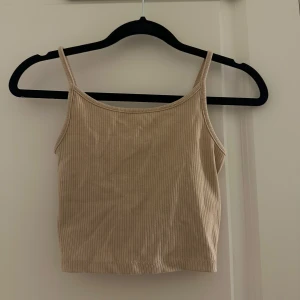 Beige ribbad linnetopp - Säljer en beige croppad linnetopp med smala axelband och ribbad struktur. Toppen har en enkel och stilren design som är lätt att matcha med olika outfits. Oanvänd!