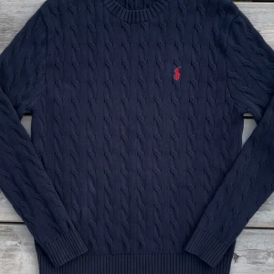 Ralph Lauren Cableknit - Navy Cableknit från Ralph Lauren med klassisk röd broderad logga på bröstet. Tröjan har rund halsringning, ribbade muddar och är tillverkad i 100% bomull. Pris kan diskuteras. Hör gärna av er vid funderingar, Mvh