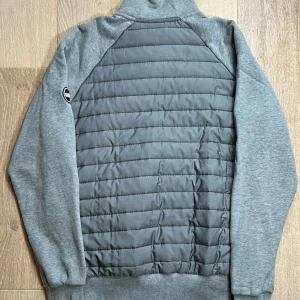 Grå quiltad jacka från colmar  - Snygg grå jacka från colmar med quiltad front och rygg, samt mjuka ärmar och muddar. Jackan har dragkedja framtill och en sportig look med logga på ärmen. Perfekt för lager-på-lager och chill vardagsstil.