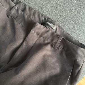 Svarta kostymbyxor från Bik Bok - Snygga svarta kostymbyxor från Bik Bok med klassisk rak passform och hällor för bälte. Byxorna har en stilren look och är tillverkade i ett mjukt material som känns bekvämt hela dagen. Perfekta för dig som gillar en clean och tidlös stil.