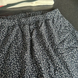 Blommig svart kjol från lager 157, stl S - Supersöt svart kjol från 157 med små vita blommor över hela tyget. Kjolen har resår i midjan och är i en avslappnad, lite lös passform. Perfekt för dig som gillar en chill och feminin stil.