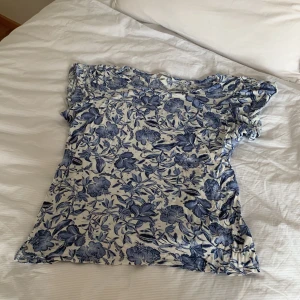 blommig blåvit blus med kort ärm - H&M - supersöt blus med blått blommönster på vit botten perfekt till en solig sommardag på stranden! använd rätt mycket men inte några större tecken på slitning! pris kan diskuteras!