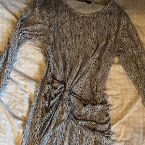 Randig långärmad klänning med knut - Snygg långärmad klänning med svartvita ränder och cool knutdetalj i midjan. Mjuk och stretchig känsla, perfekt för dig som gillar en unik look. Rund halsringning och figurnära passform.