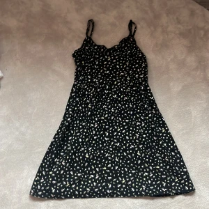 Svart blommig klänning från Divided H&M - Söt svart klänning med små vita och ljusgula blommor från Divided H&M. Klänningen har smala axelband och en lätt utställd passform. Perfekt för varma dagar eller när du vill känna dig extra fin.