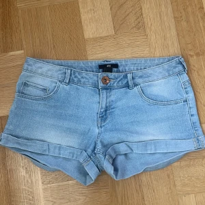 Ljusblå jeansshorts från H&M - Säljer ett par ljusblå jeansshorts från H&M med klassisk femficksdesign och uppvikta benslut. Perfekta för varma dagar och har en snygg, avslappnad look. Low waist