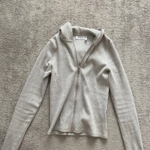 Ljusgrå ribbad hoodie med dragkedja från Weekday - Säljer en ljusgrå ribbad hoodie från Weekday i storlek S. Tröjan har lång ärm, huva och dragkedja framtill. Perfekt för en avslappnad stil och enkel att matcha med det mesta.