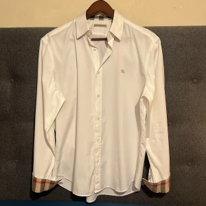 Vit skjorta från Burberry med rutiga detaljer - Säljer sommarens fetaste skjorta från märket burberry finns ingen snyggare skjorta tilll sommaren. Den är väldigt fint skick skulle säga 9,5av10 den är ny strykt och tvättad. Den kostar runt 5000kr ny! Den är något slim i passformen kom privat för mer bilder eller hör av dig vid minsta fundering😉( köparen kan få med valfritt tröja t-shirt piké eller till och med byxor) 