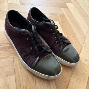 Lanvins uk 10 passar 44/45 - Snygga vinröda sneakers från Lanvin med mockaöverdel och glansiga tåhättor. Skorna har en vit sula och matchande vinröda snören. Perfekta för en stilren look. Priset går att diskutera vid snabb affär. Fråga gärna om det är något ni undrar. Dom är lite slitna.