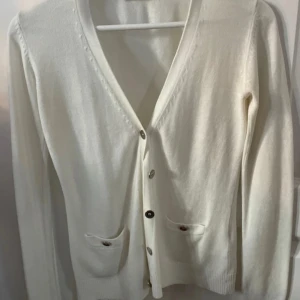 Vit kofta från Gina Tricot - Säljer en klassisk vit kofta från Gina Tricot i storlek XS. Koftan har knappar framtill och två små fickor. Perfekt att slänga över en topp eller klänning. Superenkel att matcha med allt!