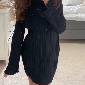 Svart glansig ribbad klänning från NA-KD - Säljer en svart ribbad långärmad klänning från NA-KD i storlek XS. Klänningen har en tight passform och är tillverkad i ett stretchigt material med fina vågiga kanter vid ärmslut och nederkant. Klänningen är i finare kvalité, tungt och glansigt