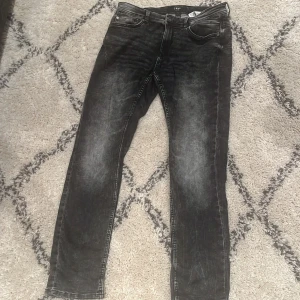 Svarta jeans från SMOG - Säljer ett par svarta jeans från SMOG med snyggt tvättad look. Klassisk femficksmodell med dragkedja och knapp i midjan. Jeansen har raka ben och passar perfekt till en avslappnad stil.