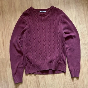 Vinröd stickad tröja från Dressmann - Säljer en vinröd stickad tröja från Dressmann i storlek L. Tröjan har kabelstickat mönster framtill, rund halsringning och ribbade muddar vid ärmslut och nederkant. Perfekt för kyligare dagar.