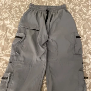 Grå cargopants - Säljer ett par grå cargopants med flera praktiska fickor och dragkedjor på sidorna. Byxorna har resår i midjan med snörning för extra komfort. Perfekta för en avslappnad och funktionell stil.