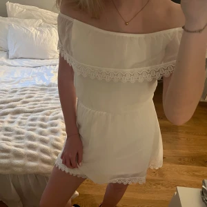 Vit offshoulder klänning med spetsdetaljer - Säljer en söt vit offshoulder klänning med fina spetsdetaljer längs överdelen och nederkanten. Resår i midjan och strechigt material. Använd en gång, i mycket bra skick!💕Passar XS/S.