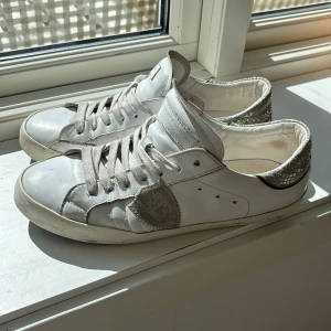 Philippe model sneakers  - Säljer ett par vita sneakers med grå snörning och glittrig detalj på hälen. Skorna har rund tå och en dekorativ grå patch på sidan. Perfekta för dig som vill ha något extra till vardagslooken.
