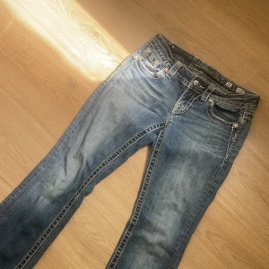 Blå jeansbyxor med broderade bakfickor från Miss Me - Säljer ett par blå jeansbyxor från Miss Me med snygga broderade detaljer och paljetter på bakfickorna. Byxorna har normal passform, är utsvängda och har klassisk femficksdesign 