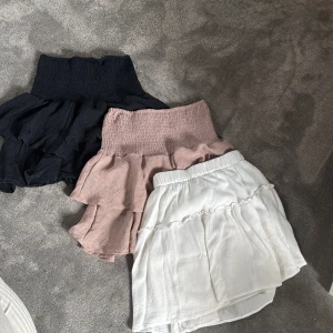 Volangkjol i tre färger - Supersöt volangkjol med smock i midjan, finns i svart, beige och vit. Kjolen har en kort längd och är tillverkad i ett lätt, luftigt tyg som ger en fin volym. 1 för 20, tre för 100