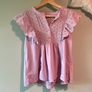 Ljuslila blus med volang  - Supersöt ljuslila blus med broderade blommor och volangdetaljer vid ärmarna. Fint skick st M