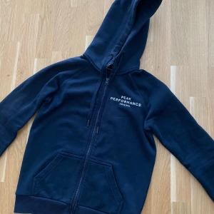 Marinblå hoodie från Peak Performance - Säljer min hoodie från Peak Performance med dragkedja och huva. Hade gärna velat ha kvar den men tyvärr har den blivit för liten. Hoppas att den kan användas utav någon annan🥰Köparen står för frakten 