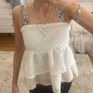 Vit volangkjol från Gina Tricot - Supersöt vit kortkjol från Gina Tricot med smock i midjan och dubbla volanger. Kjolen är gjord i ett lätt, prickigt tyg som ger en romantisk känsla. Perfekt som topp